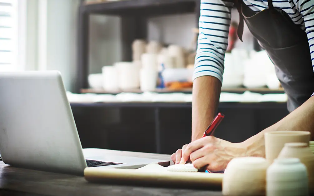 A craftsman browsing small business website on their laptop while they are in their work studio. 